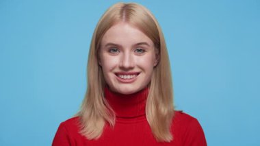 Neşeli genç bir kadının portresi. Dostane bir gülümsemesi var. Kırmızı balıkçı yaka bir kazak giyiyor..