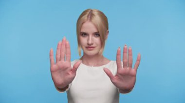 Ciddi genç bir kadın her iki elini de bir dur işareti olarak ileri doğru tutar, duraklat ya da mavi bir arkaplan oluştur..