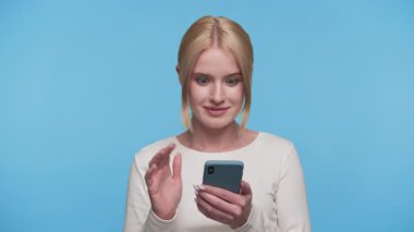 Şaşırmış genç bir kadın sevinç ve şaşkınlıkla telefonuna bakar. Mavi arka plandaki beklenmedik olumlu mesajı ya da uyarıyı kutlar..