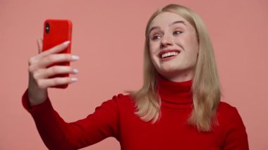 Kırmızı süveter giymiş gülümseyen genç bir kadın telefonla konuşurken pembe arka planda dikiliyordu..