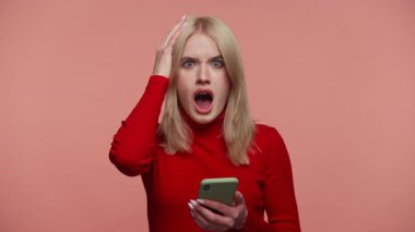 Kırmızı elbiseli genç bir kadın pembe bir arka planda elleri başının üstünde telefonuna bakıyor..