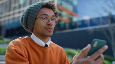 Gözlüklü ve bereli neşeli genç adam, şehirde otururken akıllı telefonuyla video görüşmesinin keyfini çıkarıyor..