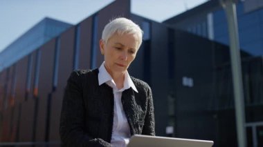 Endişeli yaşlı kadın dışarıda oturuyor ve bir sorunla karşılaştığında dizüstü bilgisayar ekranına bakıyor..