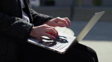 Dışarıda dizüstü bilgisayarda çalışan yaşlı bir kadın, gündüz elleri klavyede, dijital görevlere ya da uzaktan kumandalı işlere odaklanmış..