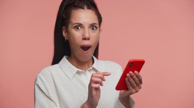 Mutlu genç bir kadın elinde akıllı bir telefonla sevinçle tezahürat yapıyor, harika haberleri kutluyor ya da pembe arka planda izole bir şekilde aldığı olumlu bir mesajı kutluyor..