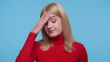 Kırmızı kazaklı sarışın kadın, mavi arka planda izole edilmiş, rahatsız edici haberler aldıktan sonra stres ya da endişeyle bakıyor..