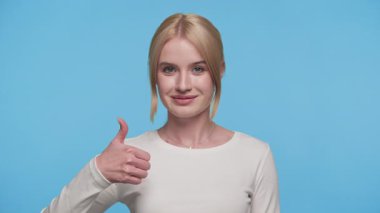 Beyaz gömlekli, kendine güvenen genç bir kadın, parlak mavi bir arkaplan karşısında gülümseyerek onay veriyor..