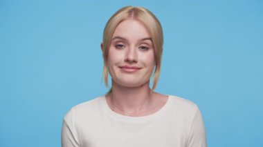 Şüpheci genç bir kadın şüpheli ya da etkilenmemiş bir ifadeyle yana bakıyor, mavi arka planda beyaz bir bluz giyiyor.