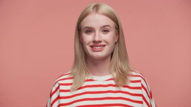 Kırmızı ve beyaz çizgili gömleğiyle sırıtan neşeli sarışın kadın stüdyoda pembe arka planda poz veriyor..
