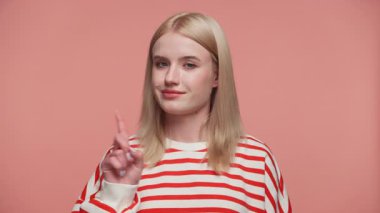 Çizgili gömlekli sarışın kadın sert bir uyarı hareketi yapıyor. Pembe arka planda ciddi bir ifadeyle parmağını kaldırıyor..