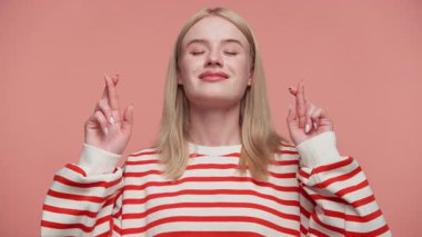 Çizgili tişörtlü sarışın kadın parmaklarını iki elinde çapraz yapar gözleri kapalı, umut ifade eder ya da şans diler..