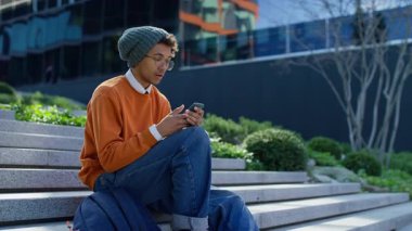 Hüsrana uğramış genç adam elinde telefonla dışarıda oturuyor, kötü habere tepki veriyor ya da testlerde başarısız oluyor..