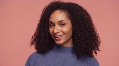 Kendine güveni tam bir genç kadın. Çekicilikle gülümsüyor. Basit bir pembe arka planda flört ya da mizah ifadesi sergiliyor..