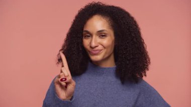 Neşeli bir sırıtışla kendine güvenen genç bir kadın bir parmağını kaldırıyor, pembe bir arka plana karşı bir uyarı veya hatırlatma öneriyor..