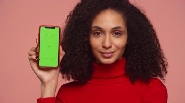Kırmızı balıkçı yakalı genç bir kadın yeşil ekranlı akıllı bir telefonu elinde tutuyor. Uygulama veya ürün modellemeleri için mükemmel..