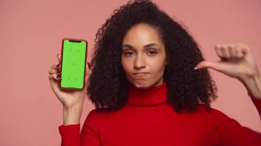 Kırmızı balıkçı yakalı, hayal kırıklığına uğramış bir kadın yeşil ekranlı bir akıllı telefonu gösterirken, bir yandan da onaylamadığını ya da memnuniyetsizliğini dile getiriyor..