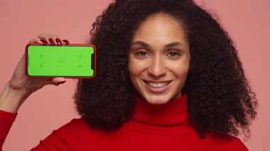 Kırmızı balıkçı yaka kazaklı mutlu bir kadın yeşil ekranlı akıllı telefonu tutuyor. Uygulama modelleri veya medya önizlemeleri için ideal..