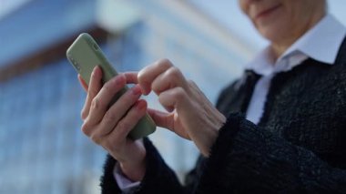 Odaklanma ve hassasiyetle akıllı bir telefonu kullanan yaşlı kadınların elleri, modern bir kentsel zemin üzerine kuruludur..
