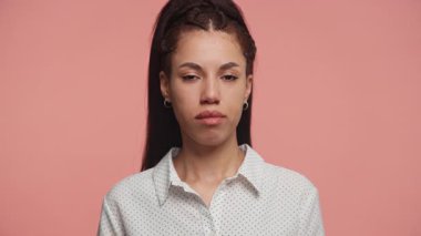 Benekli bluzlu, kendine güvenen genç bir kadın. Tarafsız bir gülümsemeyle başını sallıyor. Pembe arka plana karşı onay ya da mutabakat işareti veriyor..