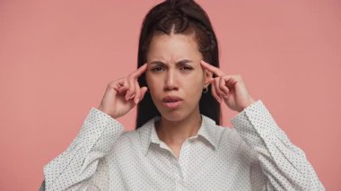 Sinirli genç bir kadın kafasını inançsızlıkla işaret ederek pembe bir arka plana karşı hayal kırıklığını ya da iğnelemeyi ifade ediyor..