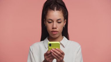 Akıllı telefonu tutan düşünceli genç bir kadın. Pembe arka plana rağmen bir mesaja nasıl cevap vereceğine karar verirken düşünceli bir şekilde başka tarafa bakıyor..