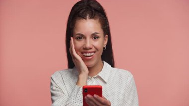 Telleri olan genç bir kadın, elinde bir telefon tutarken sıcak bir şekilde gülümsüyor. Olumlu ya da sevecen bir mesajın dokunduğu görülüyor..