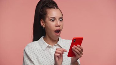 Şok edici ya da beklenmedik bir mesaja tepki veren ağzı açık ve gözleri açık genç bir kadın akıllı telefona bakıyor..