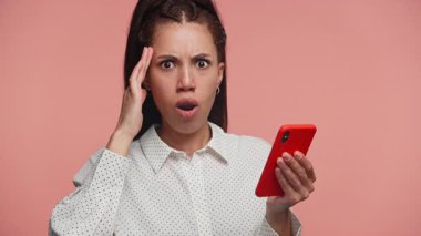 Geniş gözlü ve ağzı açık genç bir kadın bir elinde telefonla gelen mesaja olan şaşkınlığını ve şaşkınlığını ifade ediyor..