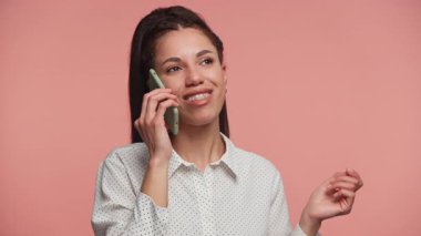 Telefonda konuşurken gülümseyen ve pembe arka planda olumlu bir sohbetin tadını çıkaran mutlu genç bir kadın..