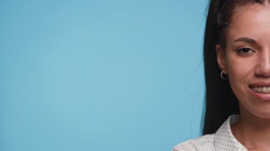 Yüzünün sadece yarısı görülebilen diş telleriyle gülümseyen genç bir kadın, açık mavi bir arka planda..