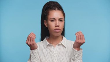 İki elini de kaldırmış ciddi bir kadın klasik bir para talebi jesti ile mavi arka plan için ödeme talebi ima ediyor..