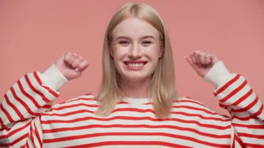 Mutlu genç bir kadın başarıyı kollarını kaldırarak ve ağzını açarak kutluyor. Pembe bir arka plana karşı heyecanını dile getiriyor..