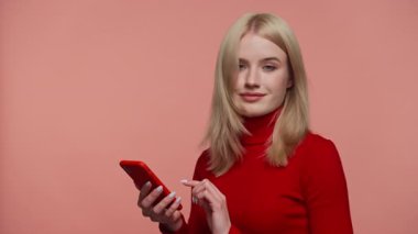Kırmızı kazaklı genç sarışın kadın akıllı telefondan süzülüyor. Tarafsız bir ifadeyle. İnce bir hoşnutsuzlukla başını sallıyor..