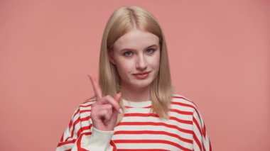 Ciddi yüzü olan sarışın bir kadın pembe stüdyo geçmişine karşı uyarı jesti olarak işaret parmağını kaldırıyor.