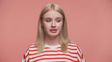 Üzgün sarışın kadın pembe stüdyo arka planında hoşnutsuz bir ifadeyle yan tarafa bakıyor.