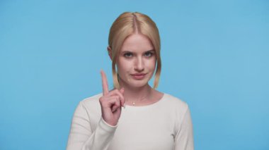 İşaret parmağı tutan genç bir kadın ya da ciddi yüzlü bir hatırlatma hareketi, mavi arka plan