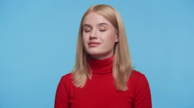 Kırmızı balıkçı yaka kazaklı sarışın kadın mavi arka plana poz veriyor, stüdyo portresi.