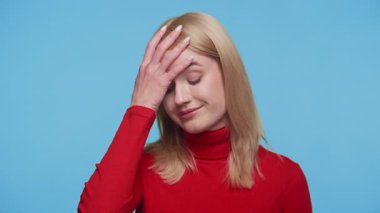 Kırmızı kazaklı sarışın kadın facepalm hareketi yapıyor. Stüdyodaki hayal kırıklığını ve pişmanlığını dile getiriyor.