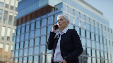 Modern kentsel iş bölgesinde akıllı telefondan konuşan takım elbiseli olgun bir kadın.
