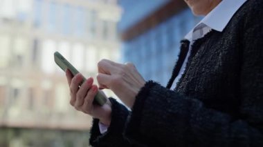 Güpegündüz ofis binasının önünde akıllı telefondan yazı yazan gülümseyen son sınıf öğrencisi.