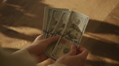Ahşap bir yüzey üzerinde el ele tutuşup, birkaç yüz dolarlık banknotları sayarak....