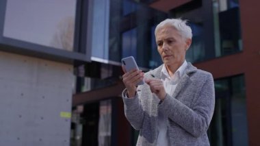 Olgun bir kadın, şehir merkezinde akıllı telefondan kötü haberler okurken şok olmuş gibi görünüyor.