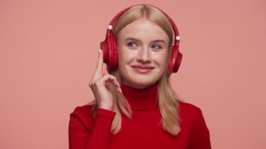 Kırmızı kulaklıklı, kırmızı kazaklı, pembe arka planda izole edilmiş mutlu genç bir kadın.