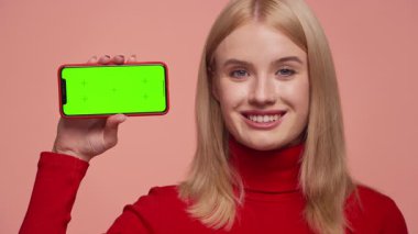 Kırmızı elbiseli mutlu kadın yeşil ekranlı telefonu yatay olarak tutuyor. Uygulama ya da video modeli için ideal.