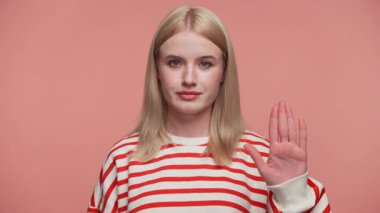 Pembe arka planda ciddi bir ifadeyle dur işaretinde el ele tutuşan sarışın kadın.