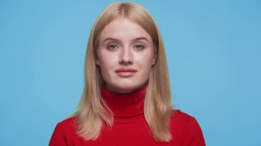 Ciddi bir genç kadın portresi, sarı saçlı, kırmızı balıkçı yakalı, mavi bir arka planı var..