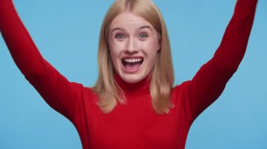 Kırmızı balıkçı yakalı neşeli genç kadın heyecandan çığlık çığlığa yumruklarını kaldırarak mavi arka plana karşı zaferini ilan ediyor..