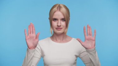 Beyaz gömlekli genç sarışın kadın iki elini de avuçlarında açık tutarak mavi arka planda dur ya da dur işareti veriyor..