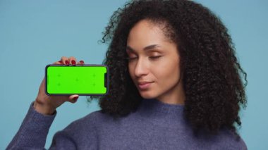 Mutlu genç kadın yeşil ekranlı akıllı telefonu tutarken onaylıyor, uygulama modelleri veya reklamlar için ideal..