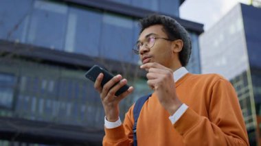 Modern bir şehir ortamında açık havada yürürken akıllı telefonuyla hoparlör kullanıyor..